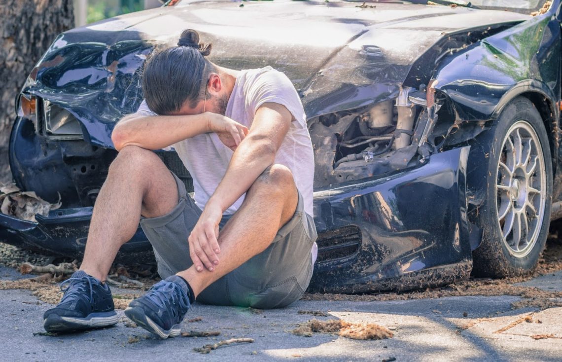 A depressed man sitting beside his wrecked car