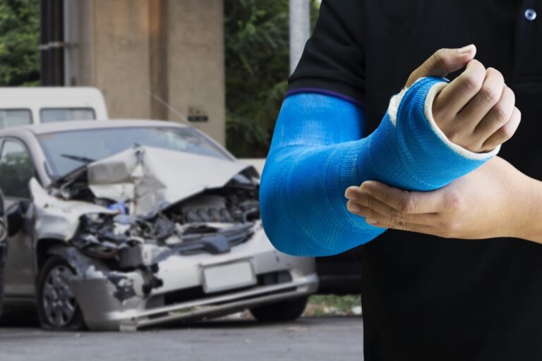 Man holding his arm in a cast with car accident in background