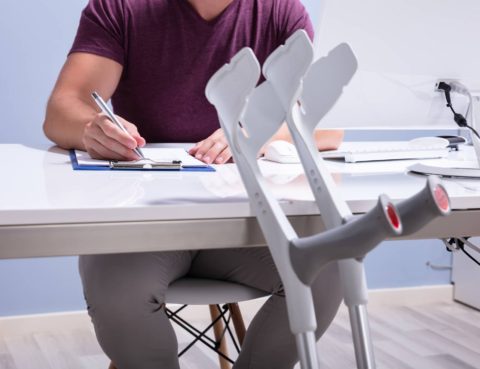 close up of crutches and man filling out form on table