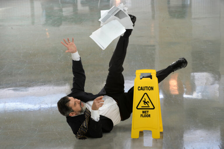 senior businessman falling on wet floor in front of caution sign