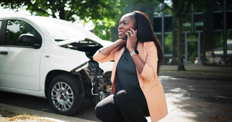 Woman on cell phone with damaged vehicle in background